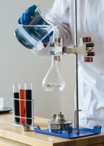 Químico de cultivos vertiendo líquido claro en cristalería frágil en el centro científico