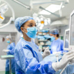 A nurse in full PPE in a surgery setting is looking at a monitor