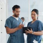 2 healthcare workers consulting an ipad in a hospital setting