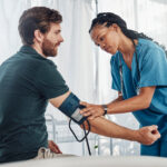 Nurse, doctor and man with blood pressure test in hospital for heart health or wellness. Healthcare, hypertension consultation and medical physician with patient for examination with sphygmomanometer