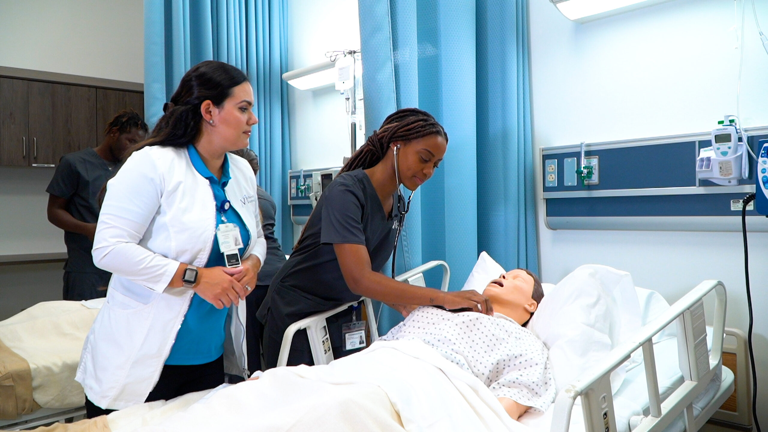 An FVI nursing instructor watches as a nursing student performs health checks on a patient simulator in a skills lab