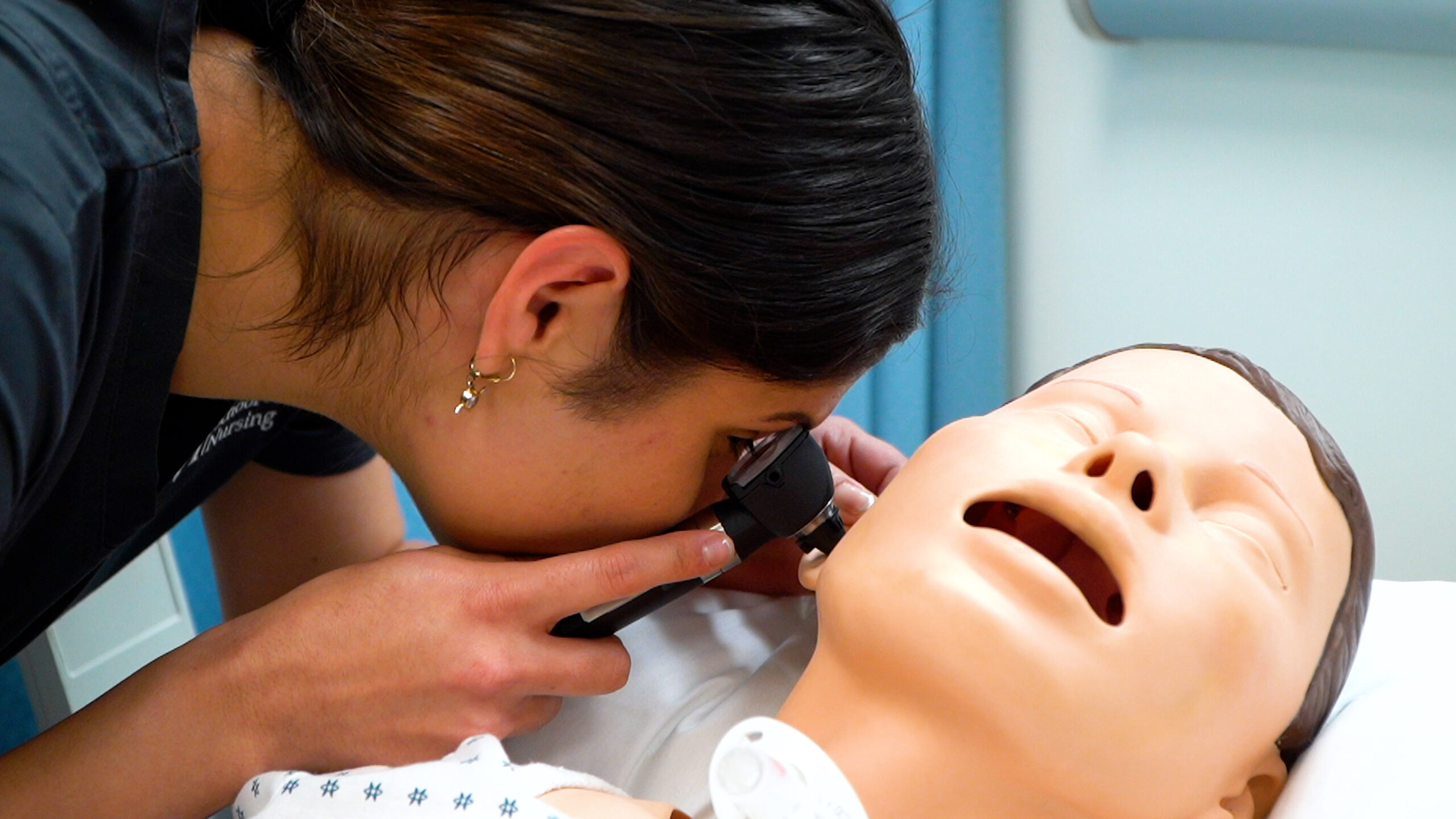 A nursing student using an instrument looks inside the ear of a patient simulator