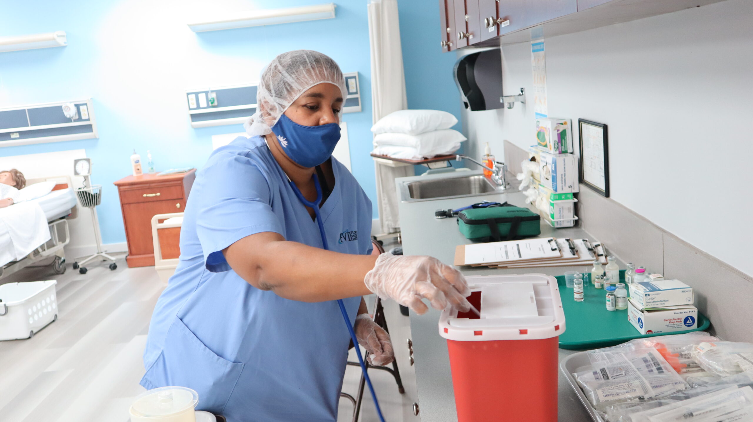 A healthcare student safely disposes of medical waste in a biohazard collection container in a skills lab
