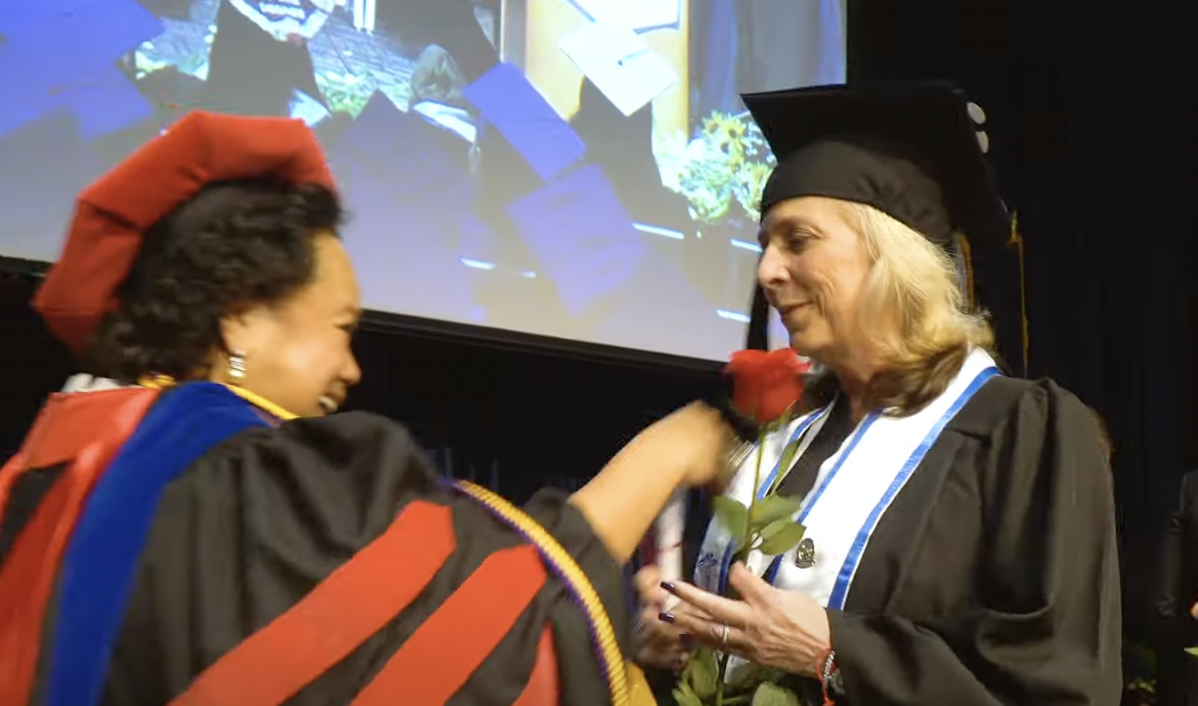 FVI's director of nursing hands a red rose and congratulates an FVI nursing student at graduation on stage