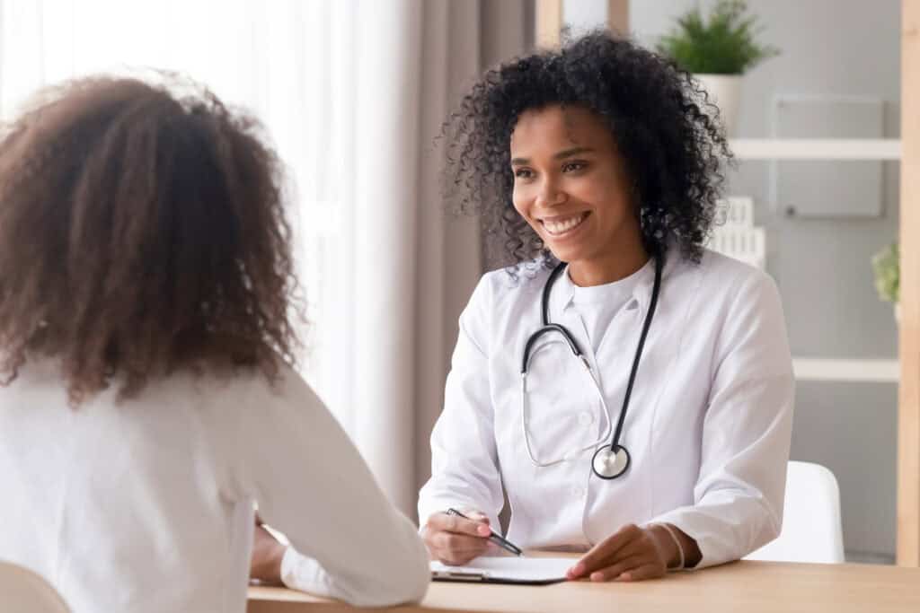 Smiling african female doctor talking to patient making notes