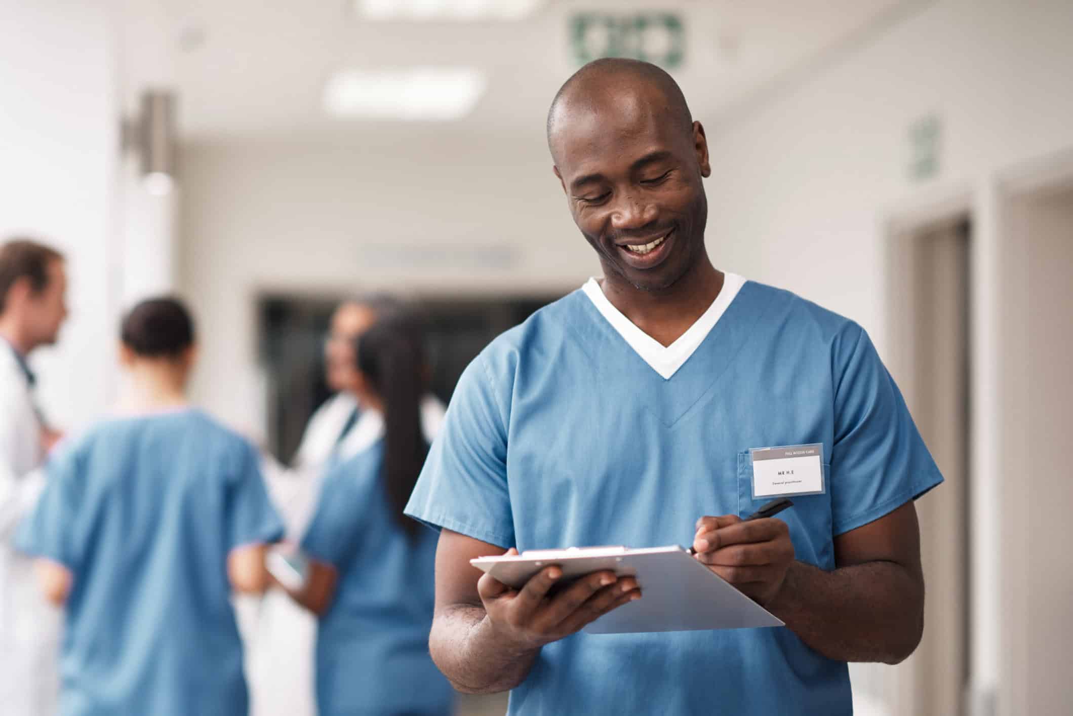 Insurance documents, clipboard and a black doctor writing patient info. Clinic healthcare employee or male nurse with a smile, consulting a medical chart. A man in scrubs, smiling in hospital hallway