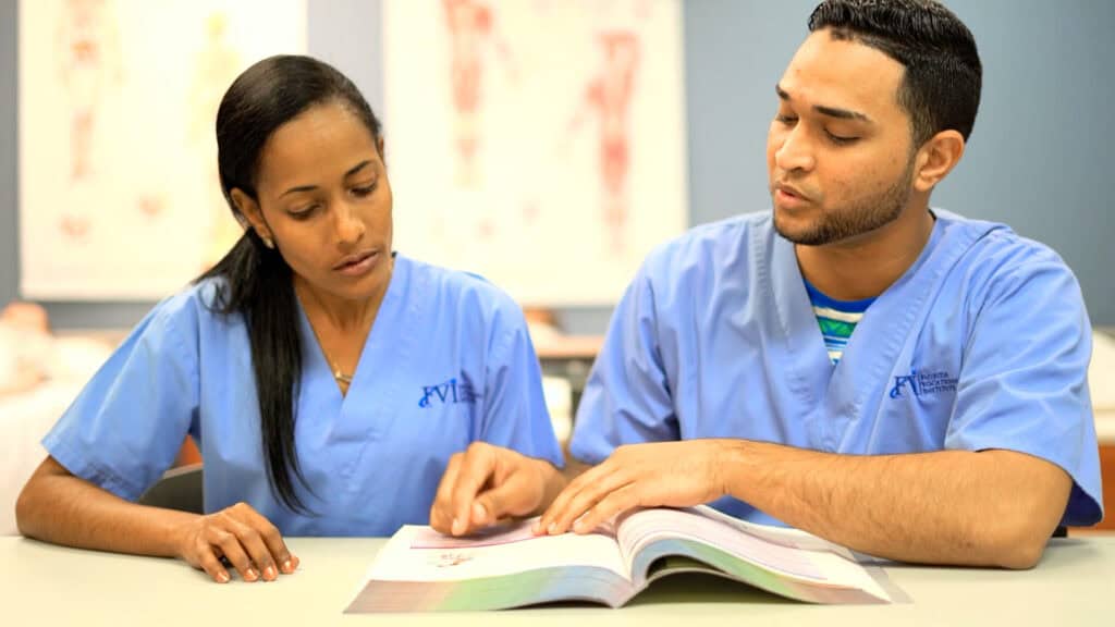 2 students studying from a book in a classroom