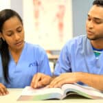 2 students studying from a book in a classroom