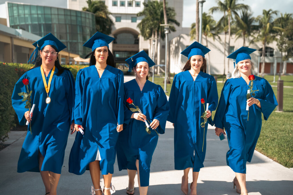 5 FVI graduates outside graduation in blue caps and gowns holding red roses