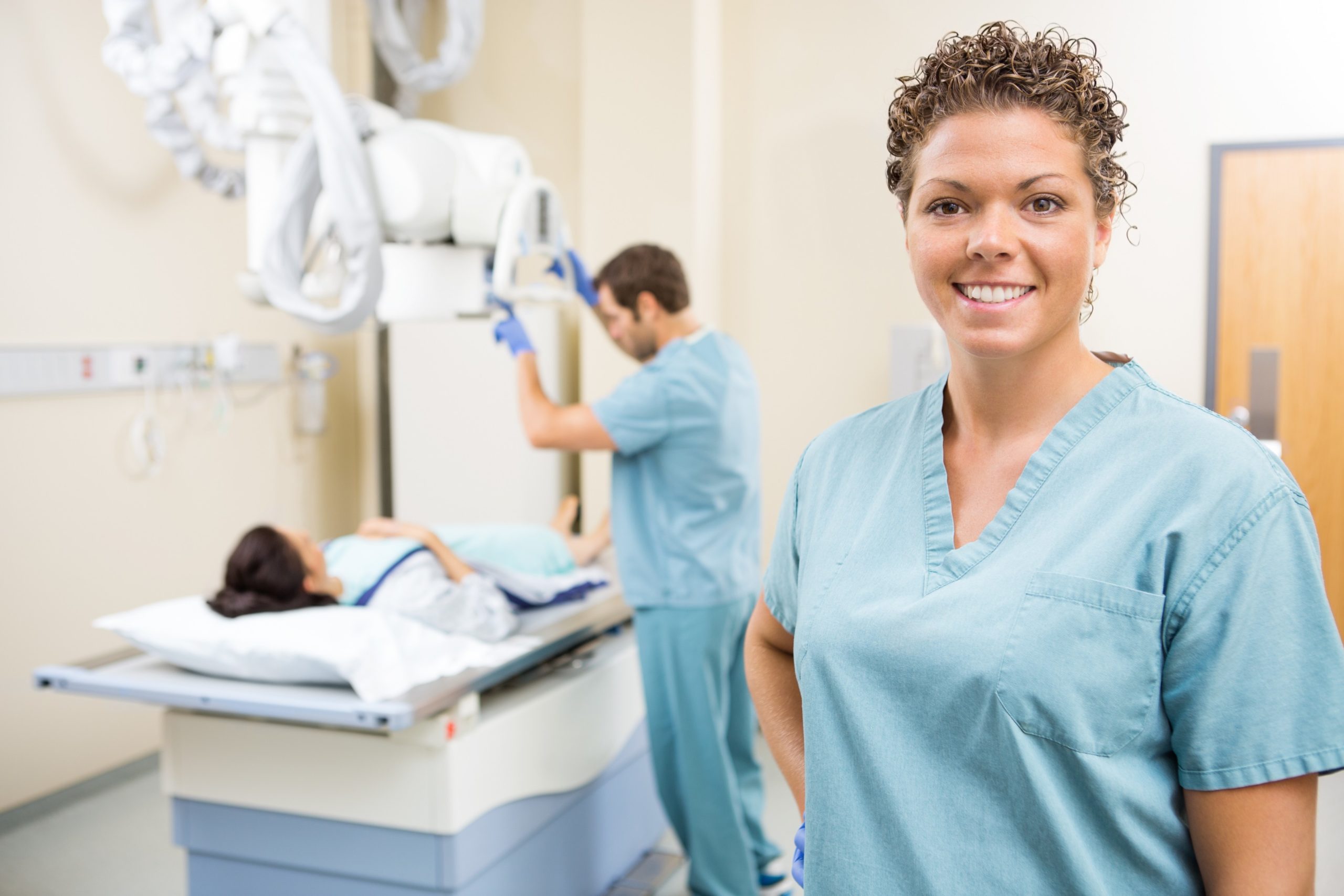 Portrait of radiologist smiling while colleague preparing patient for xray in examination room