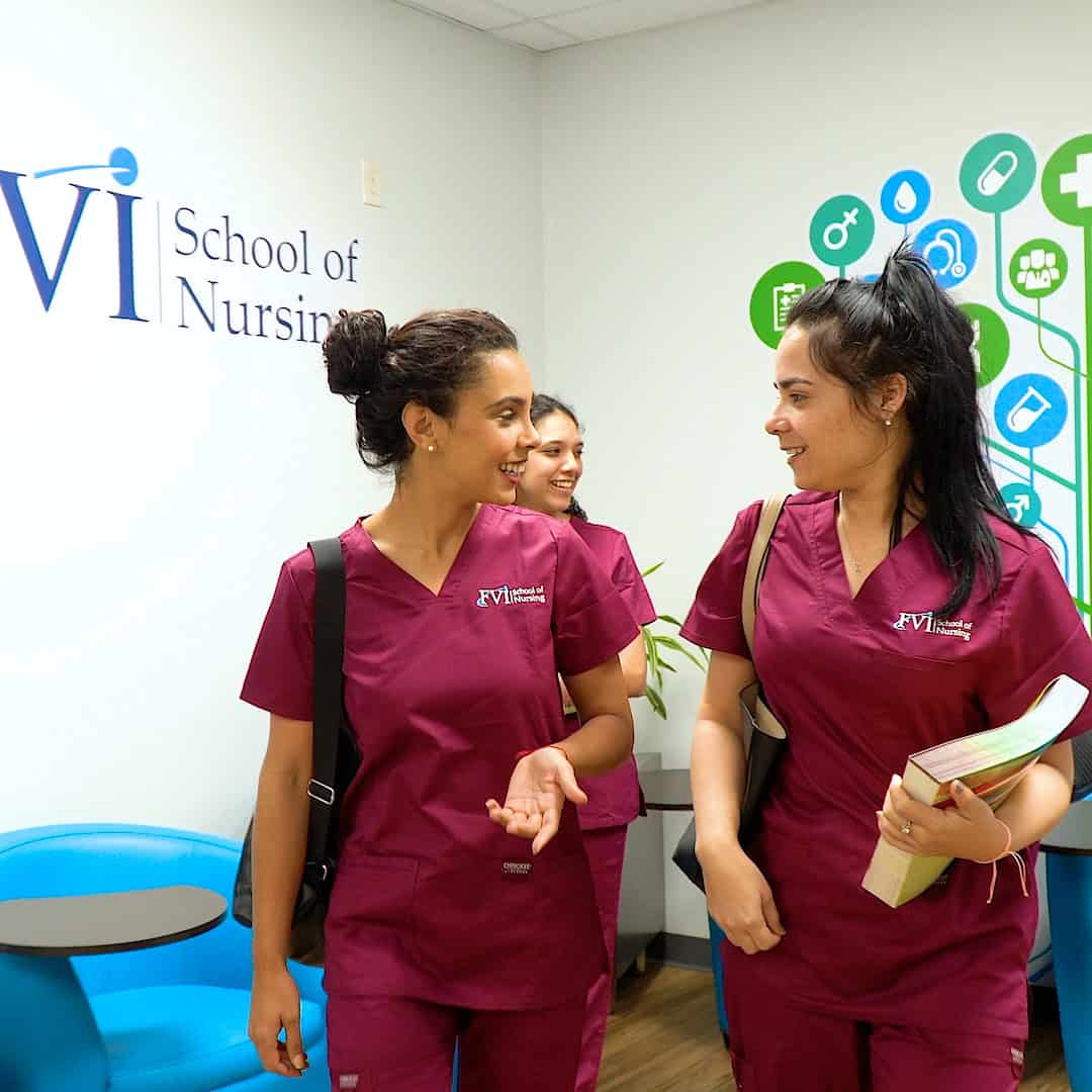 Three Practical Nursing students smiling and talking at FVI School of Nursing, wearing burgundy uniforms.