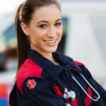 Smiling EMT professional standing in front of an ambulance with a stethoscope.